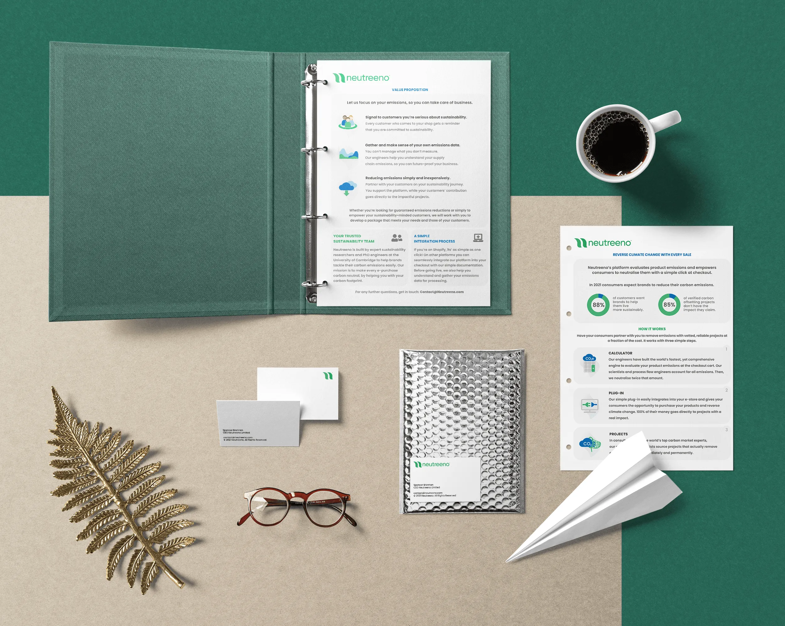 Desk setup with open binder, black coffee, paper plane, glasses, leaf decor, and branded business cards.