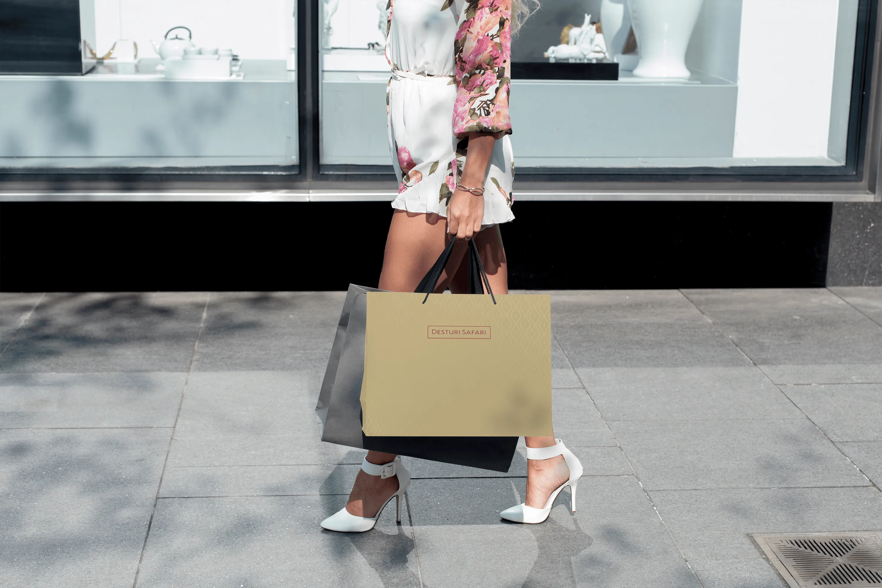 Woman in floral dress and white heels walking with shopping bags on city sidewalk.