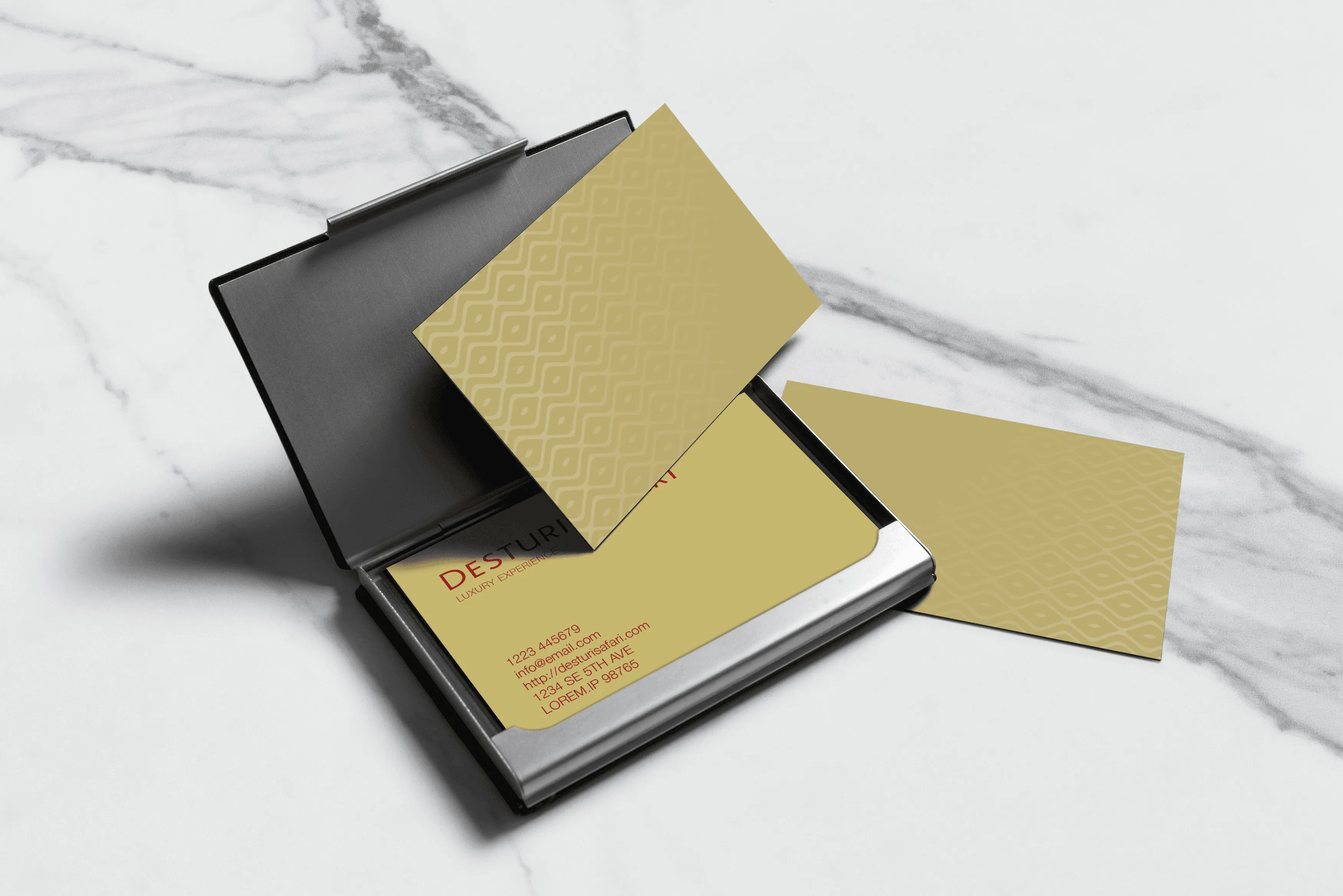 Metal business card holder with gold cards featuring subtle pattern and contact info on marble surface.